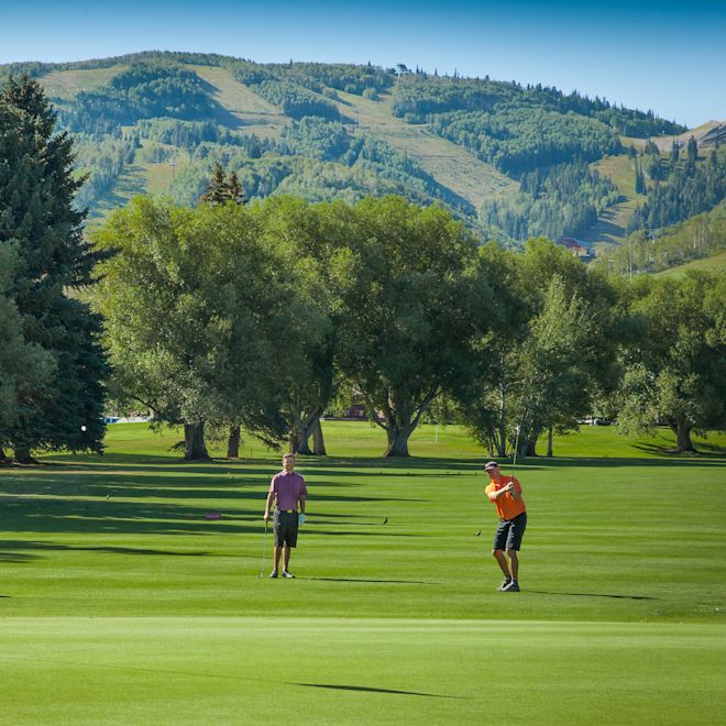 Oameni jucându-se de golf într-o zonă cu munți