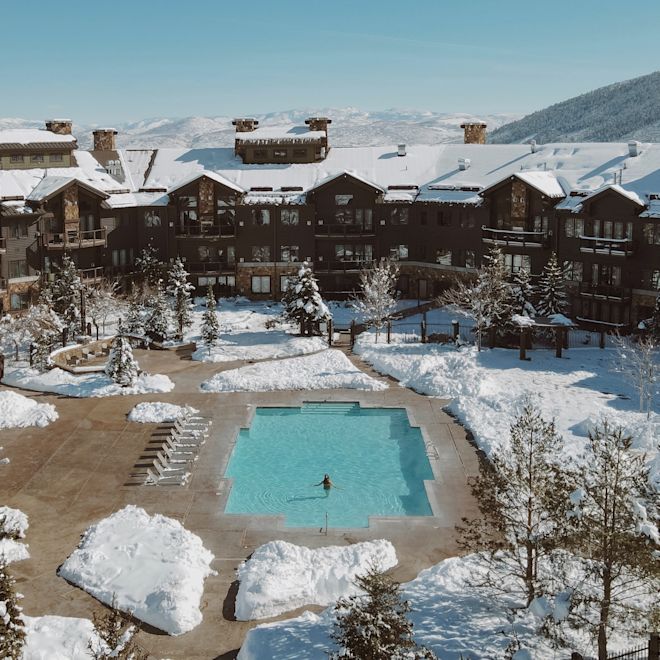 Femeie într-o piscină exterioară într-o zi de iarnă înzăpezită, cu vedere spre exterior spre hotel