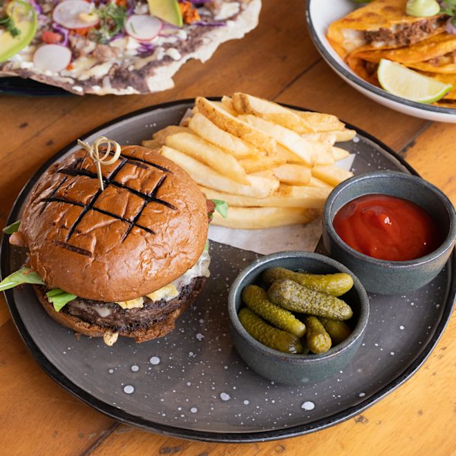 Sandviș, cartofi prăjiți, murături și sos pe o masă la Carbon Chiringuito