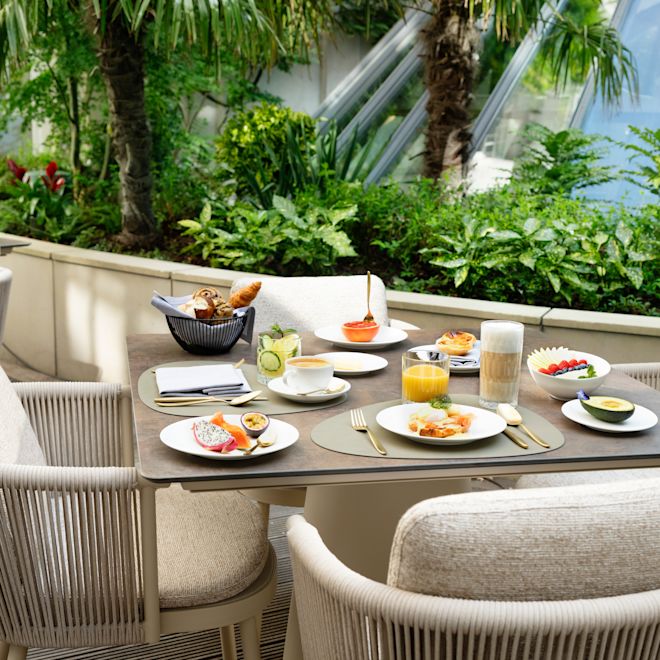 tavolo da pranzo accanto alle piante verdi, piatti per la prima colazione, cocktail a base di succhi di frutta