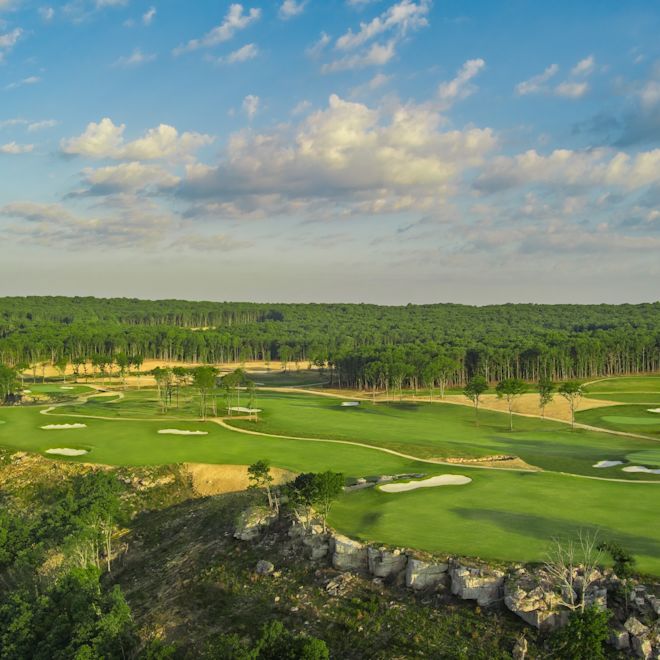 Aerial view of golf course with cliff edge, tree line, and water traps