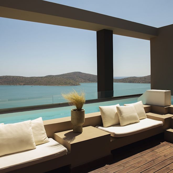 Outdoor seating area with shared pool access, white cushioned benches, and a view of the ocean and mountains.