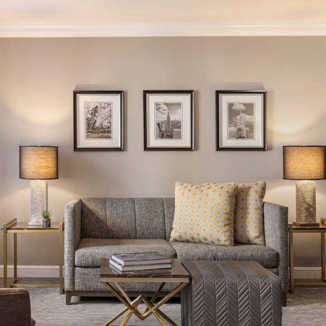 Junior suite lounge area including a sofa with yellow and white decorative pillows, end tables with lamps, a small table, ottoman, and chair.