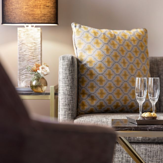 The end of the sofa, in the lounge area, with yellow, white, and gray decorative pillows and a tray with champagne and glasses on the table.