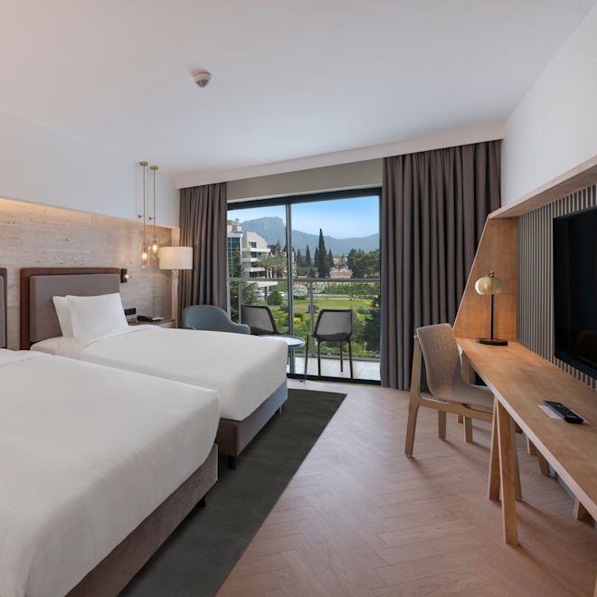 Zimmer mit zwei Einzelbetten, Fernseher, Schreibtisch und Balkon