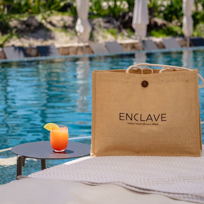 Sac enclave sur une chaise longue près de la piscine et cocktail sur une table