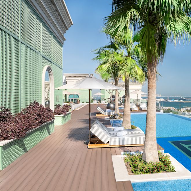 Outdoor Pool Area with Lounge Seats under Umbrellas, Palm Trees and Beach View
