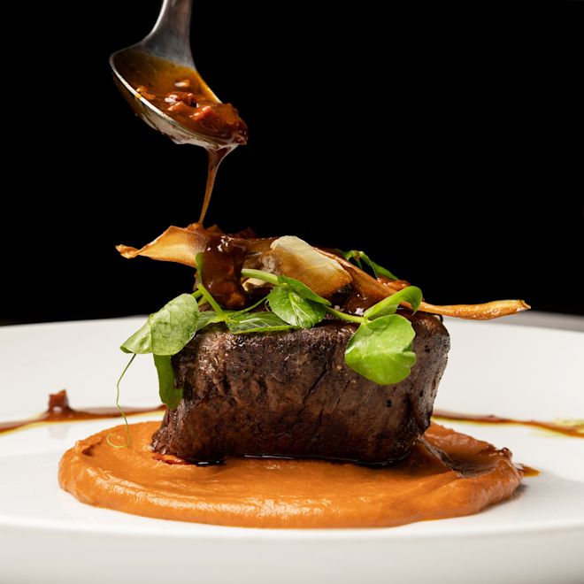 Filet Mignon dinner entree presented with finishing sauce on white plate