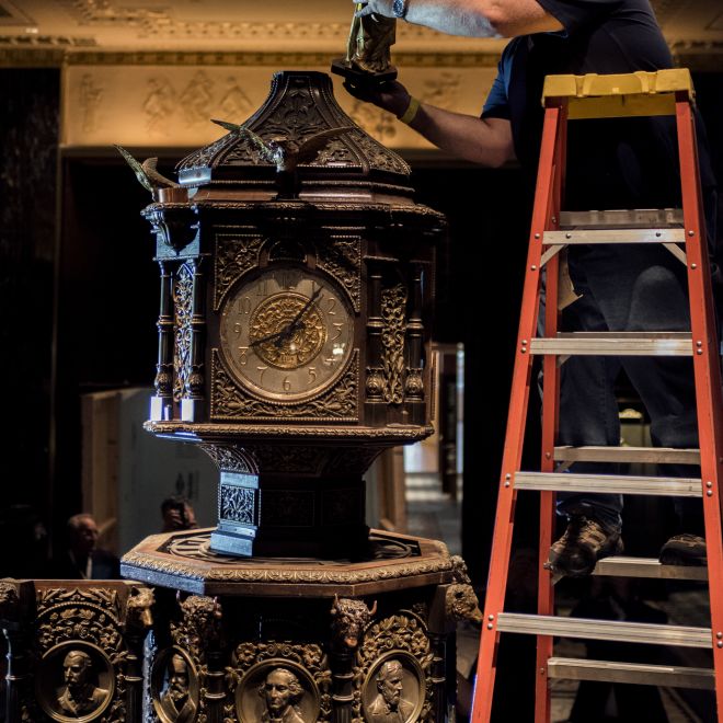 homme sur une échelle ajoutant la statue de la liberté au sommet de l'horloge du hall Waldorf Astoria