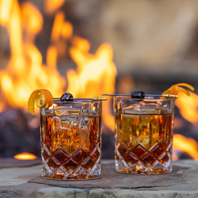 Două pahare de cocktail pe o masă cu funcție de incendiu în fundal