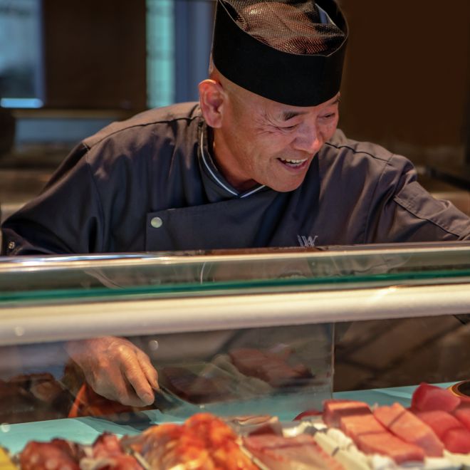 Chef Making Sushi Rolls with a Variety of Fish in Clear Covered Bar