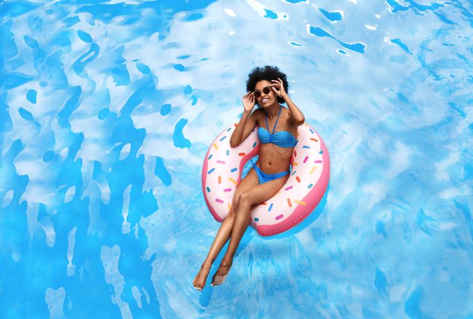 Black woman in blue bikini swimming on inflatable ring at pool during tropical vacation.