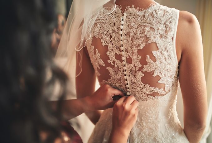 Bride having the back of her lace wedding dress buttoned up