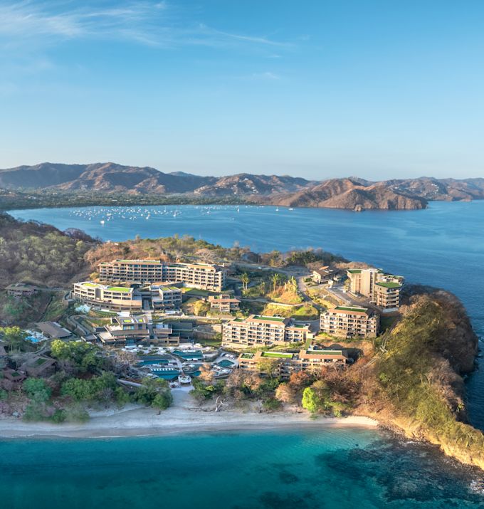Drone shot of hotel exterior from a distance, showing surrounding ocean and coast