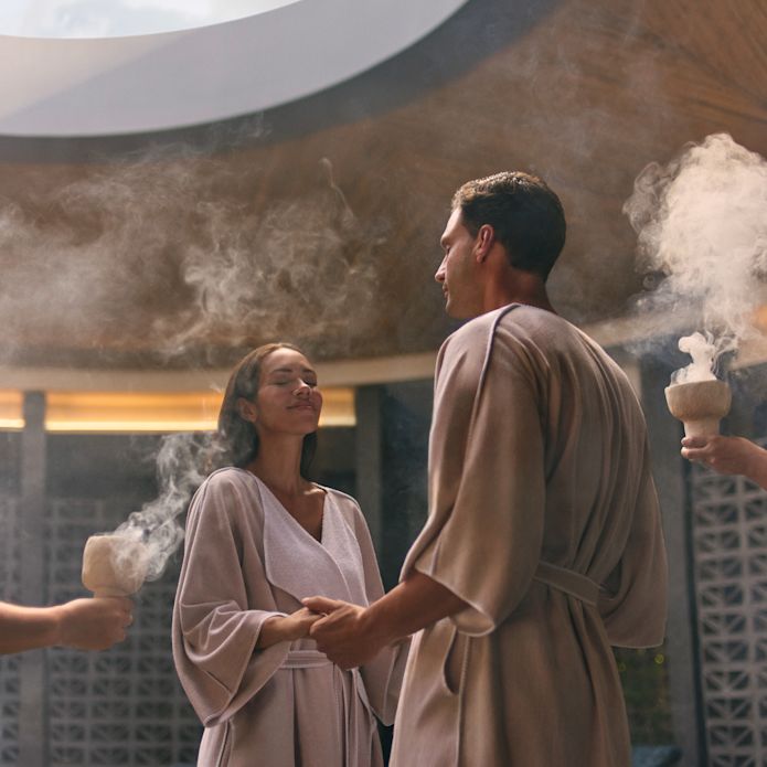 Una donna e un uomo si tengono per mano in piedi nella spa e i dipendenti tengono le ciotole con l'incenso del fumo