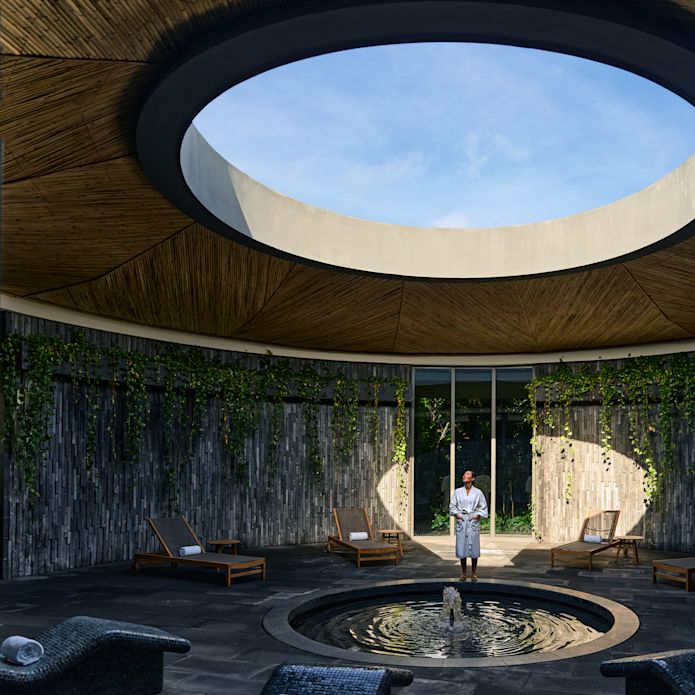 Área del spa con un haz de luz que ilumina una parte circular de la pared. Una persona está de pie en la luz