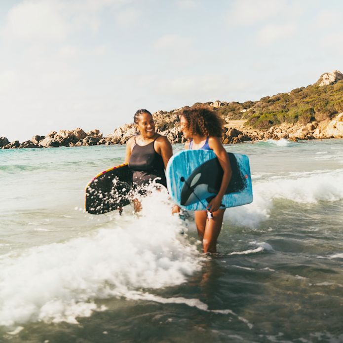 Women walking through along beach with surf boards