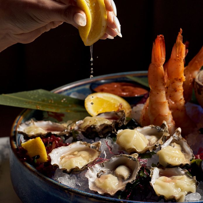 Woman Adding Lemon to an Oysters and Shrimp Dish at Nube Restaurant