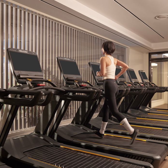 健身中心設有心肺功能鍛鍊器材，以及在跑步機上跑步的女士