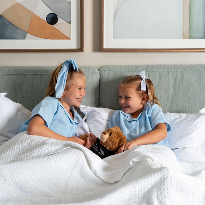 Dua anak perempuan di tempat tidur dengan boneka beruang