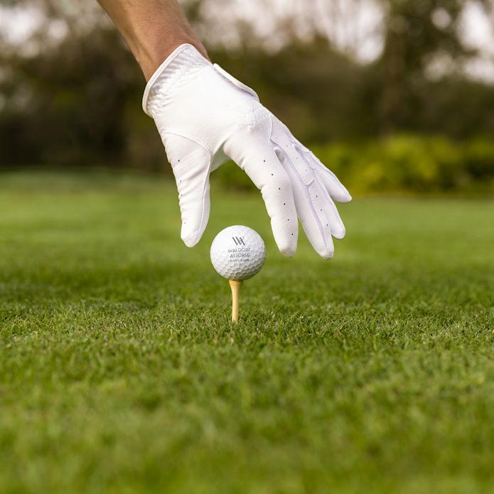 Une main gantée plaçant la balle de golf Waldorf sur le tee