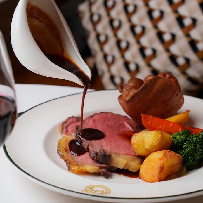 Person Pouring Sauce on a Plate with Meat and Potatoes at The Court