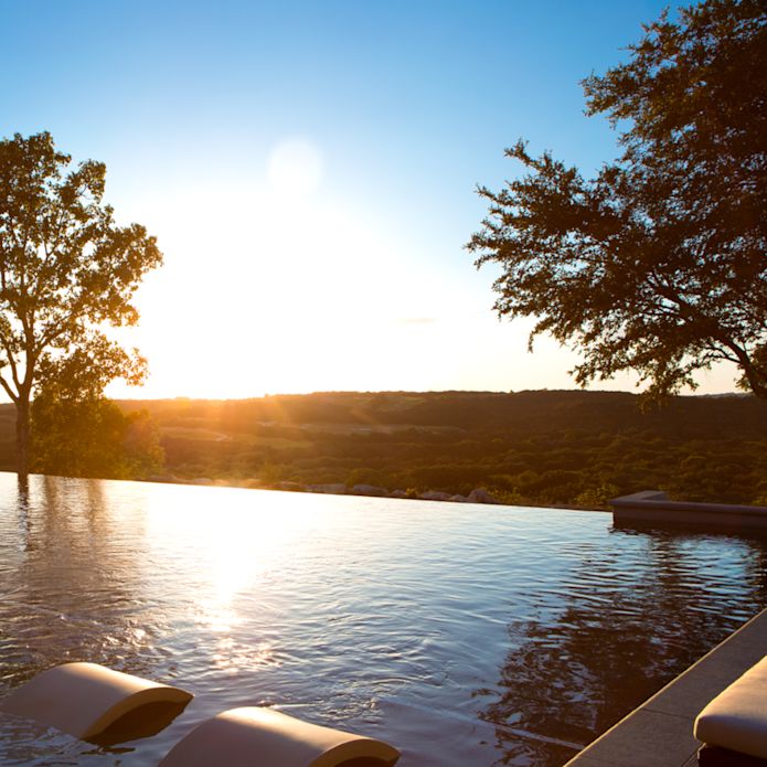 View of outdoor swimming pool with large trees at sunrise