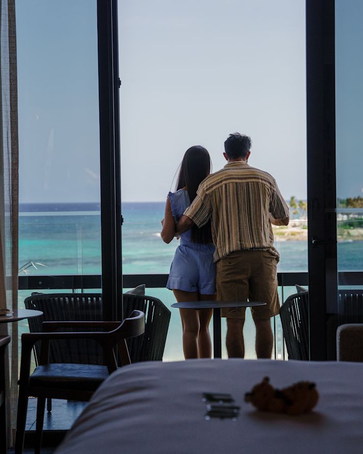 Casal em pé na varanda, de trás para frente, com vista para o mar