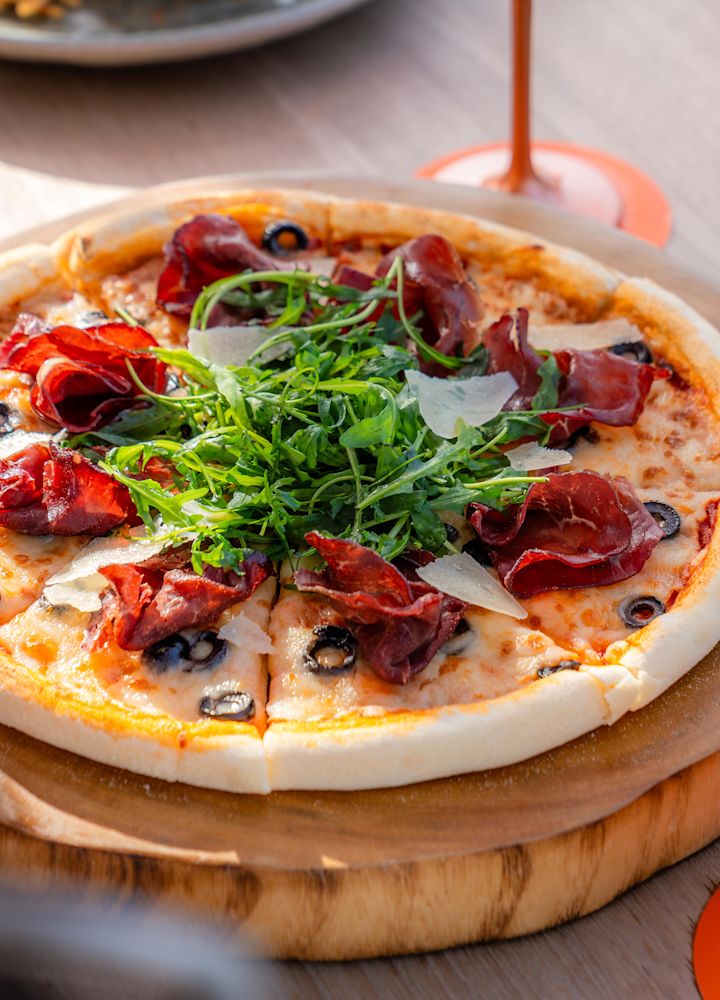 Pizza na kulatém dřevěném servírovacím talíři s koktejlem po boku