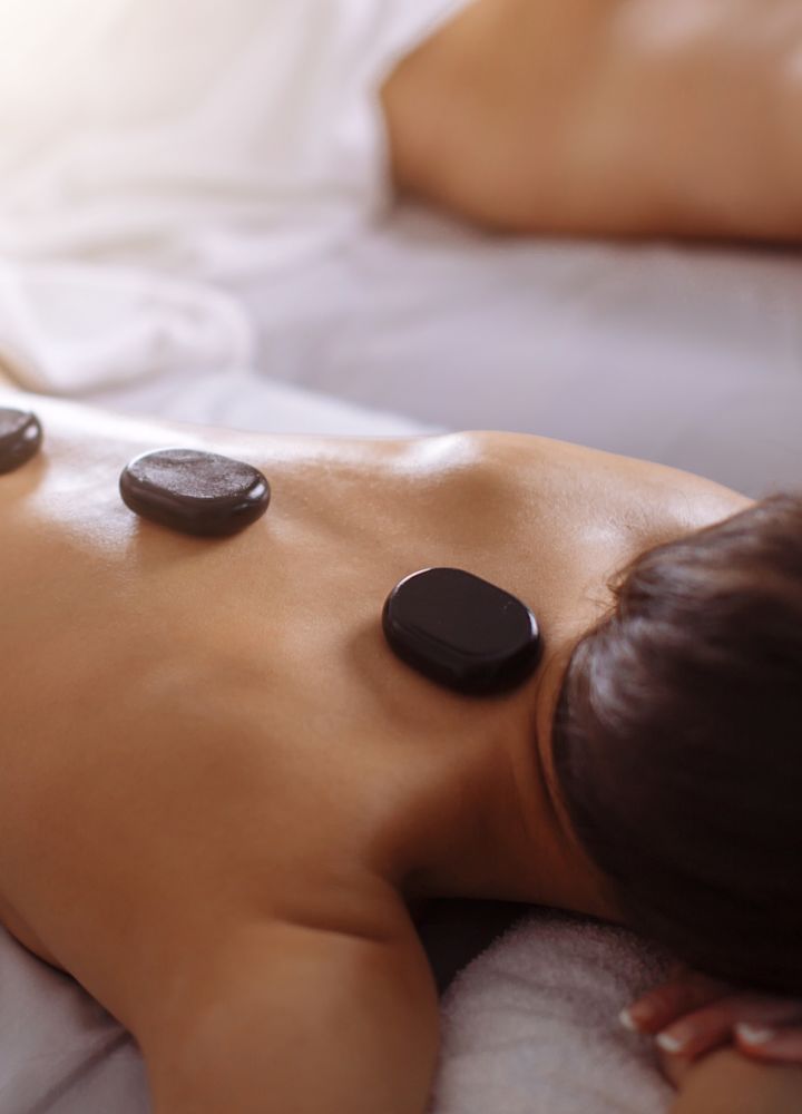 Wanita berbaring di tempat tidur perawatan dengan bebatuan panas yang ditempatkan di sepanjang tulang belakang