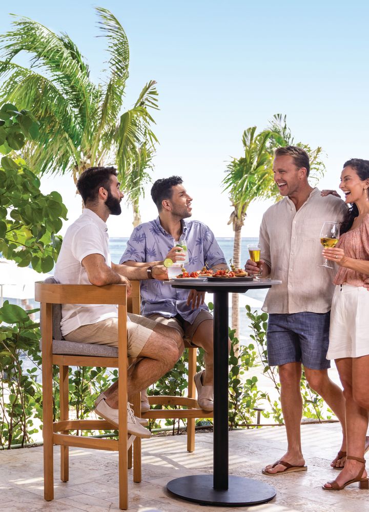 Four people share drinks and food by the ocean