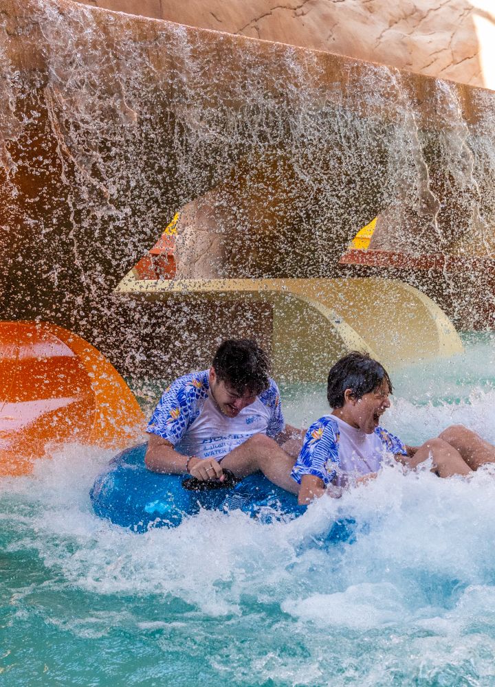 two teenagers riding an inner tube on an outdoor pool slide