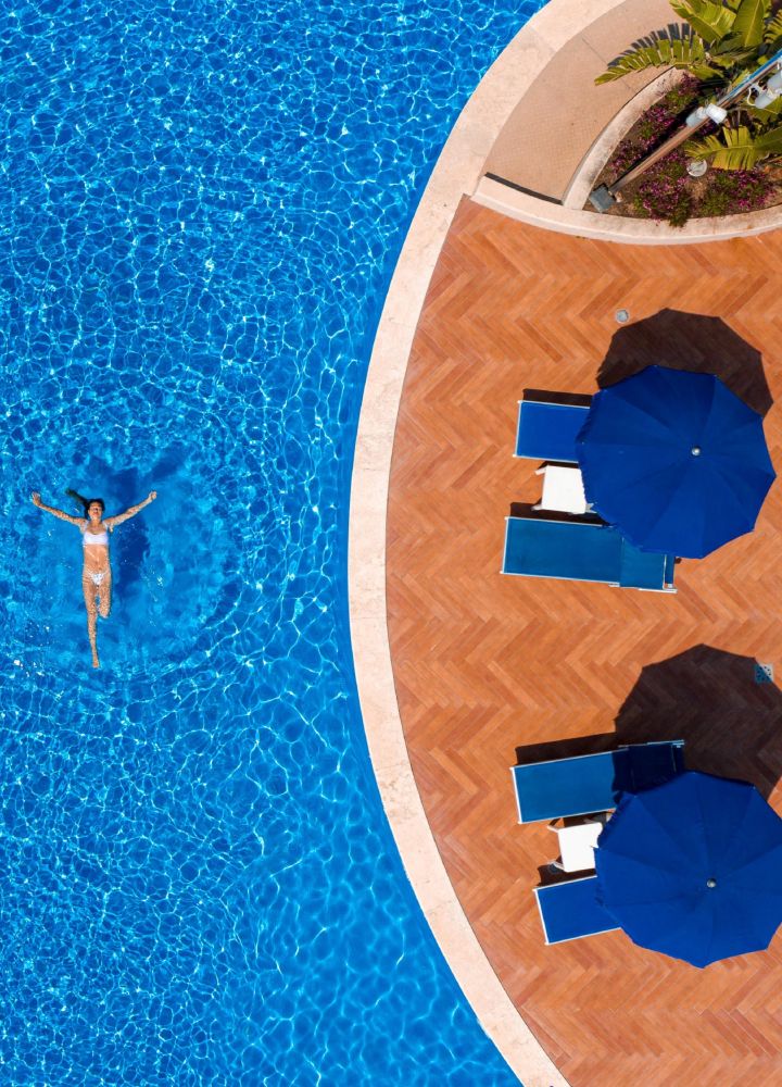 Donna che nuota in un'ampia piscina esterna con salotto sotto gli ombrelloni