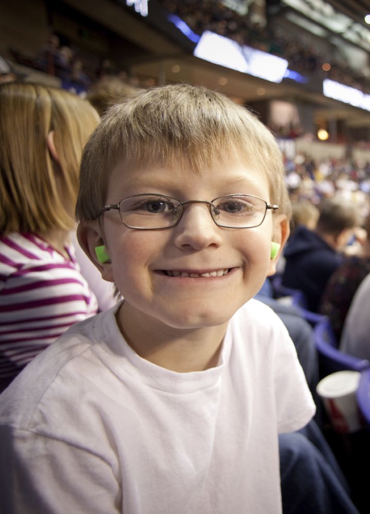 Young Boy Wearing Eyeglasses and  Green Earplugs at Sporting Event