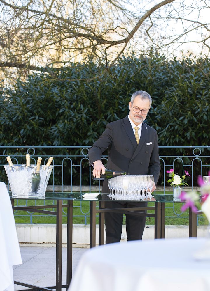 Un membru al echipei de sex masculin turnează șampanie în canapele, pregătindu-se pentru participarea oaspeților la un eveniment în aer liber.