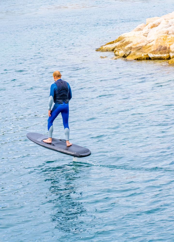 Person using an electric foil on the ocean near rocks