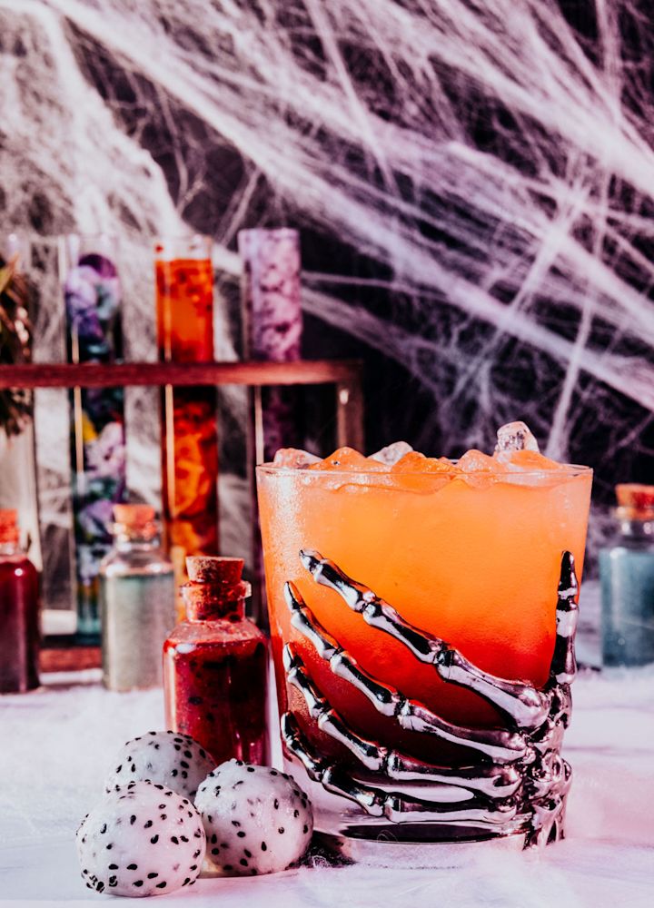 Metallic Skeleton Hand Holding a Halloween Cocktail Glass on a Table