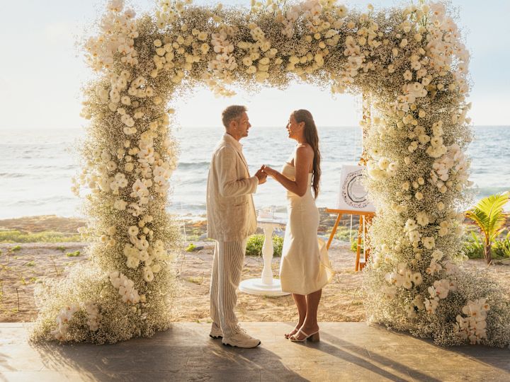 Paar hält die Hände unter dem Blumenbogen am Wasser