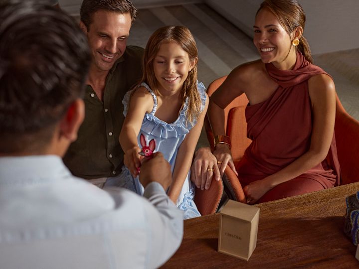 Un membru al echipei dăruiește unei fete o figurină mică din lemn roz de jucărie, în timp ce părinții ei privesc zâmbind.