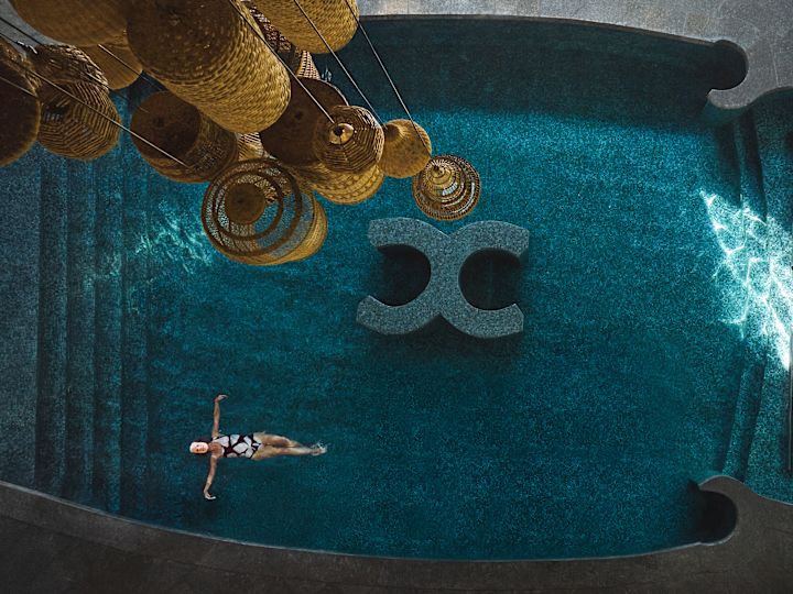 Birdseye view of one woman floating on her back in the pool relaxing while another woman rests in one of the loungers in the pool