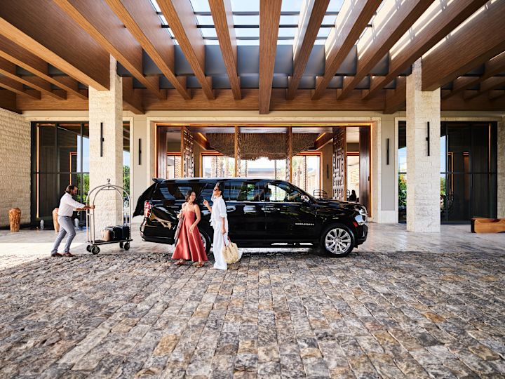 Two woman walking past car as staff member attends to luggage