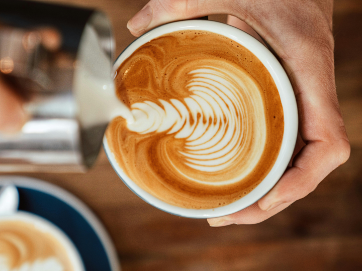 ساقي يضيف تصميمًا رغويًا في فنجان قهوة في مقهى الصالة