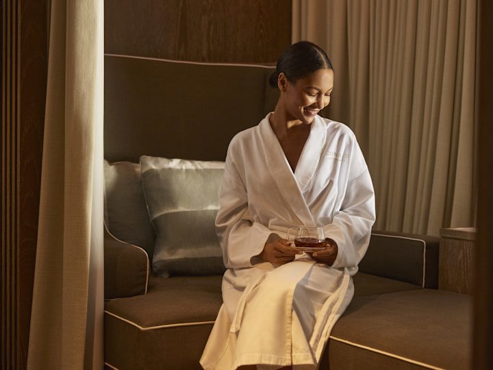 Woman in white bathrobe relaxing in comfortable seating area with drink