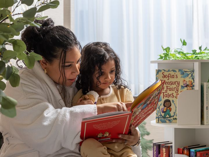 Mum and child reading book next to bookshelf