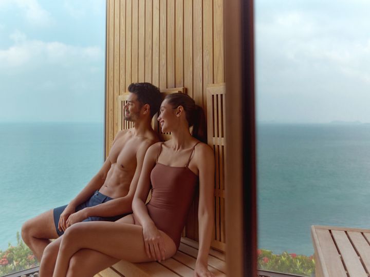 Man and woman relaxing on wooden seating looking out at ocean view