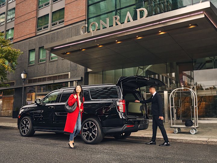 Femme marchant dans une voiture noire, tandis que le membre du personnel retire ses bagages de la voiture