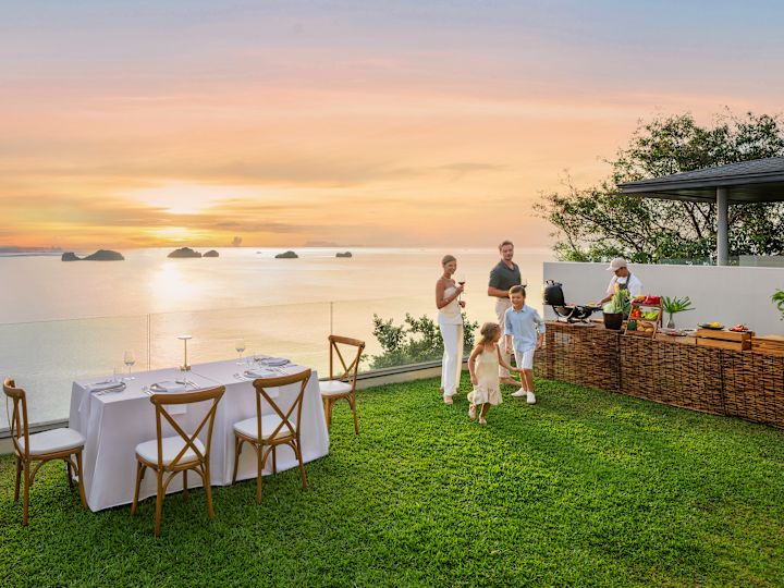 Family dining outdoors at a private BBQ event in a lawn with beach view at sunset