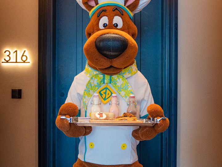 Eine Person, die ein Scooby-Doo-Kostüm trägt, trägt ein Tablett mit Lebensmitteln