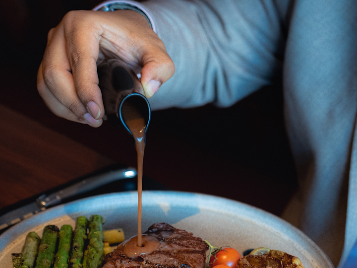 Person, die Sauce auf ein Steak mit Spargel im The Directors Club zaubert