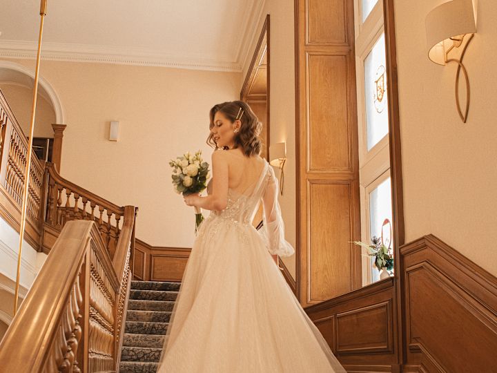 Die Braut steht auf einer Treppe und hält einen Strauß weißer Blumen